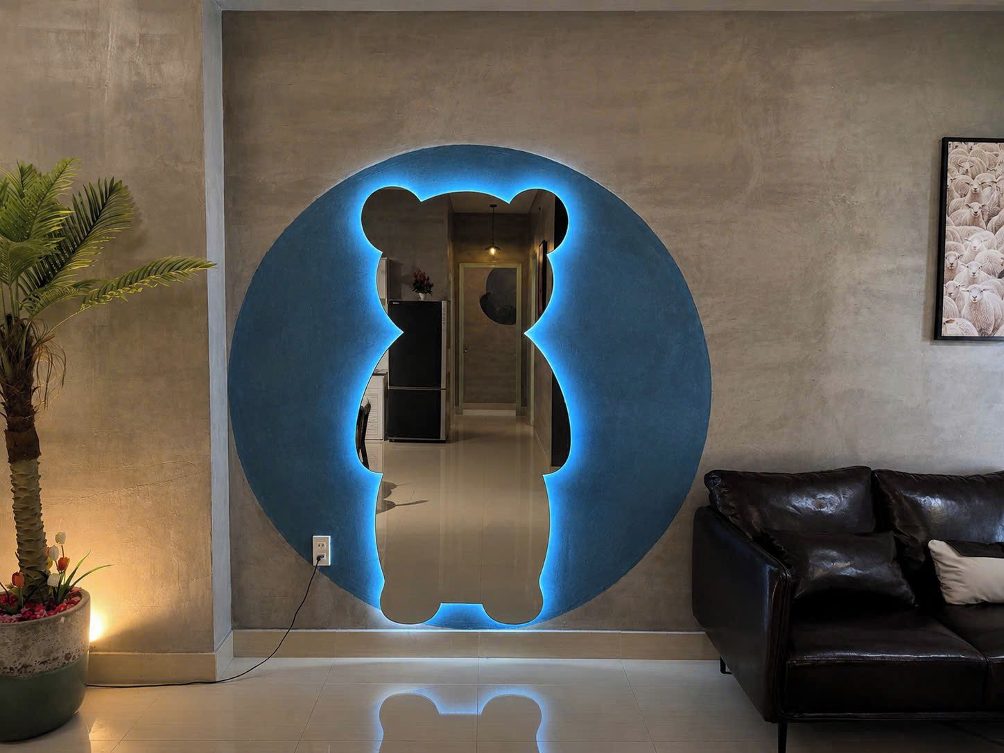 A room with a circular mirror reflecting a bear silhouette, a potted plant, a sofa, and a framed picture on the wall.