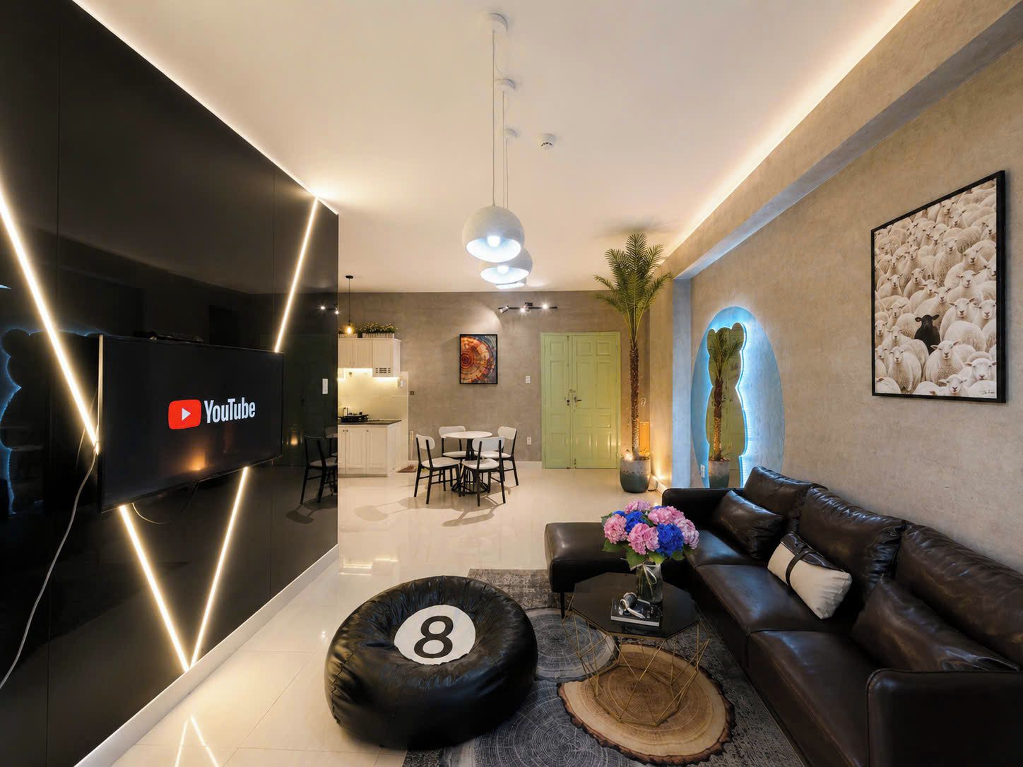 En moderne stue med et fladskærms-tv, en sort lædersofa, et sofabord med blomster og et spiseområde i baggrunden.
