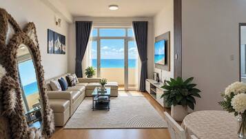 Un salon moderne avec un canapé, une table basse et une vue sur la mer grâce à de grandes fenêtres.