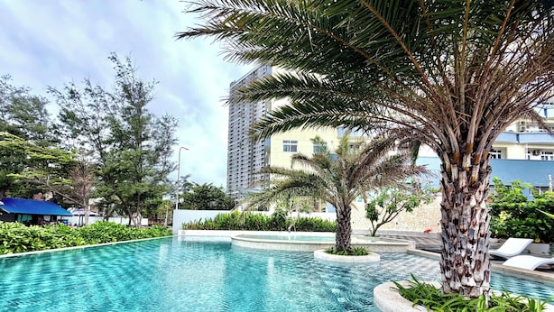 A clear swimming pool with a palm tree and lounge chairs. - MOC AN COLLECTION-Blue Sea Beachfront VT (Vung Tau)