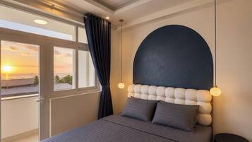 A bedroom with a large bed, a view of the sunset, and a modern headboard.