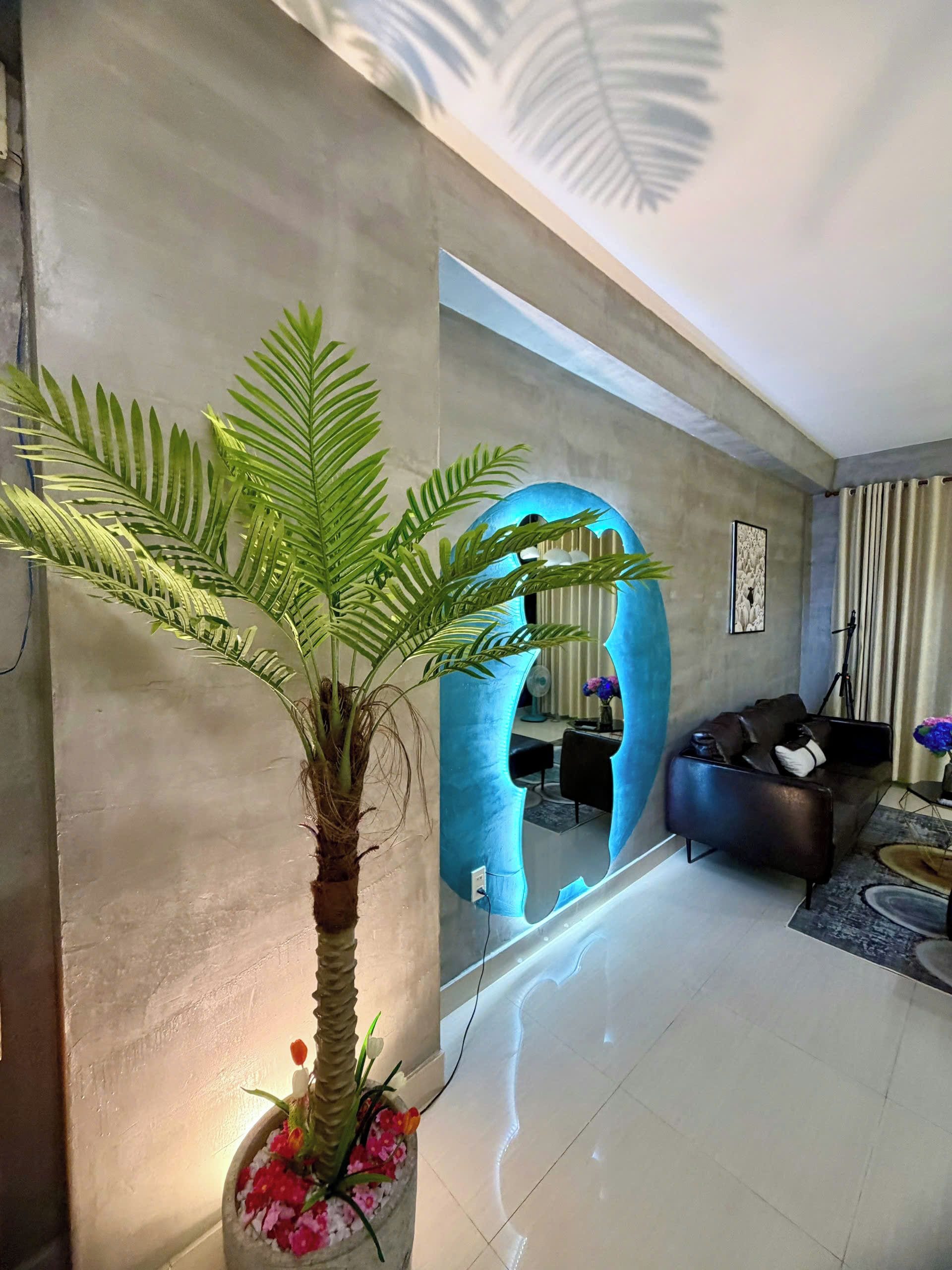 A modern living room with a large potted plant, a sofa, and a unique blue archway.