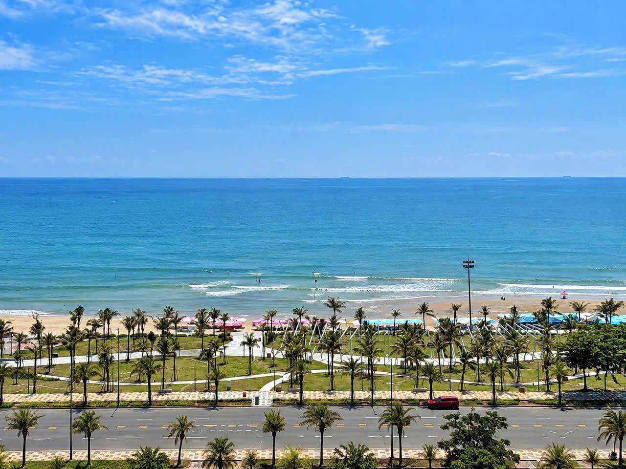 A coastal view with a beach, palm trees, and a clear sky.