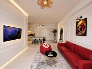A modern living room with a red sofa, a black coffee table, and a large TV mounted on the wall. - MOC AN COLLECTION-Blue Sea Beachfront VT (Vung Tau)