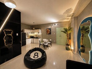 A modern kitchen with white cabinets, a dining area with a round table and chairs, a black bean bag chair with the number 8, and a green door. - MOC AN COLLECTION-Blue Sea Beachfront VT (Vung Tau)