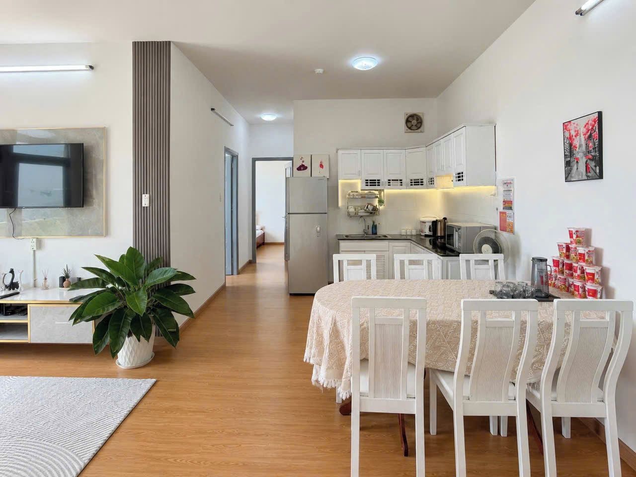 Una cocina moderna con armarios blancos, un comedor con sillas blancas y una planta grande en maceta.