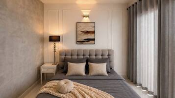 Une chambre à coucher avec une tête de lit capitonnée, une lampe de chevet, un grand tableau et une fenêtre avec des rideaux.