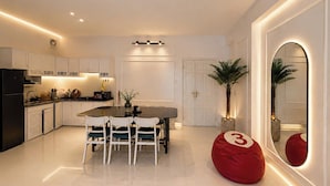 A modern kitchen with white cabinetry, a dining table with chairs, a red bean bag, and a large mirror with a number '3' on it. - MOC AN COLLECTION-Blue Sea Beachfront VT (Vung Tau)