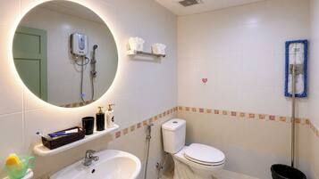 Baño con lavamanos, inodoro y ducha. Se observa un espejo con luz, un perchero y un bote de basura.