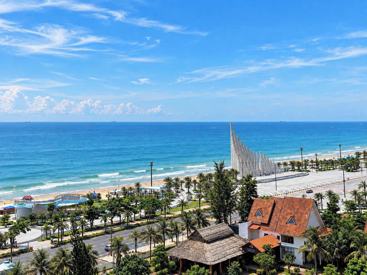 A coastal view with a beach, palm trees, and a distinctive modern building with vertical lines.