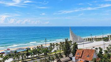 A coastal view with a beach, palm trees, and a distinctive modern building with vertical lines.
