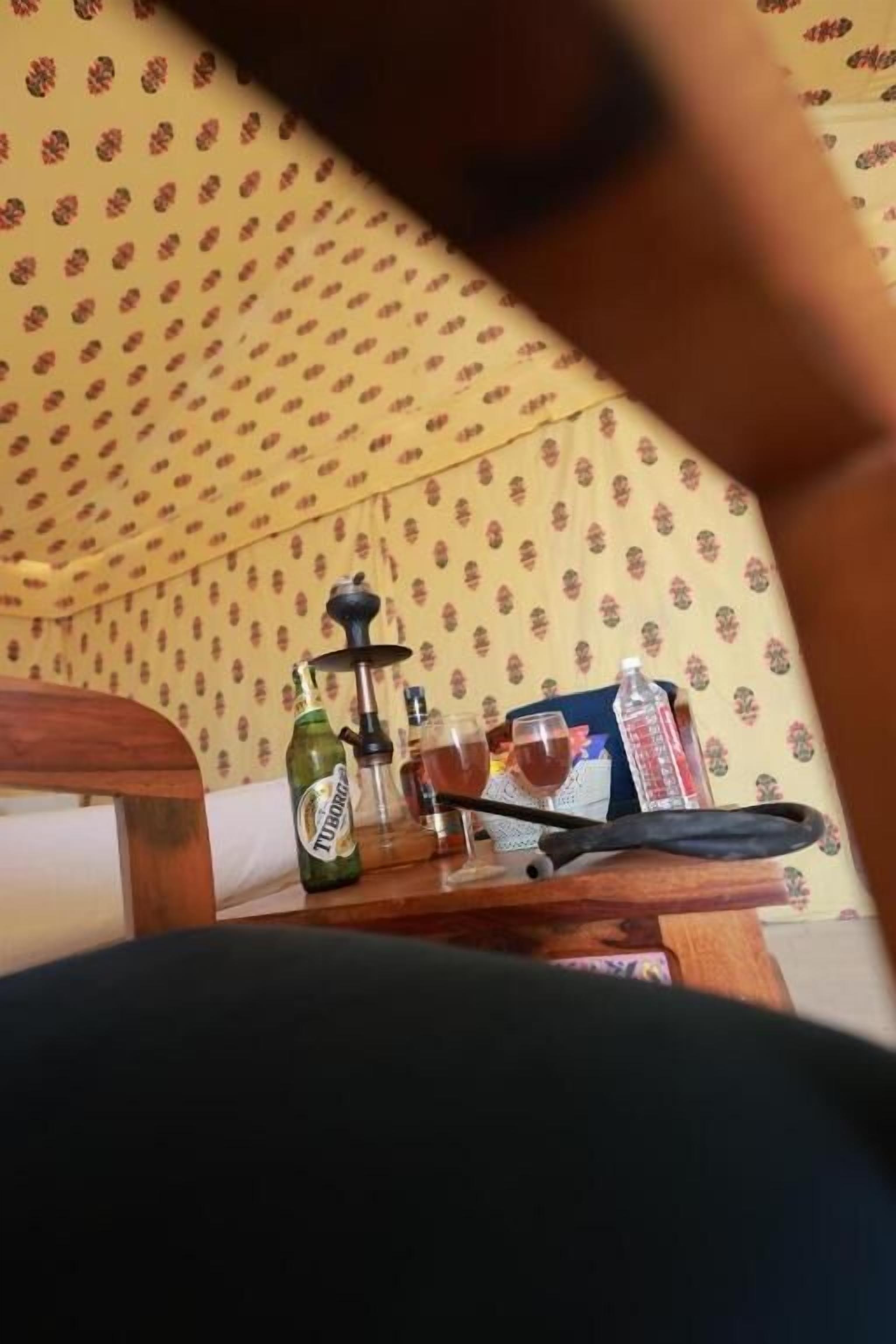A room with a patterned wallpaper, a table with a bottle, a glass, and a hookah.