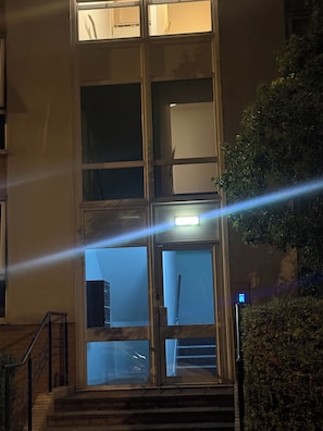 Ein mehrstöckiges Gebäude mit einem zentralen Eingang, großen Fenstern und einer Treppe, die zum Eingang führt.
