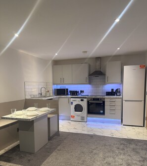 A modern kitchen with built-in appliances, a central island, and under-cabinet lighting. - Cosy Modern 3 Bedroom Apartment with Secure Private Carpark (Leeds)