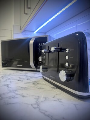 A kitchen with a modern appliance, a microwave, and a toaster on a marble countertop. - Cosy Modern 3 Bedroom Apartment with Secure Private Carpark (Leeds)
