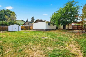 A residential area with a single-story house, a fenced yard, and a large tree.