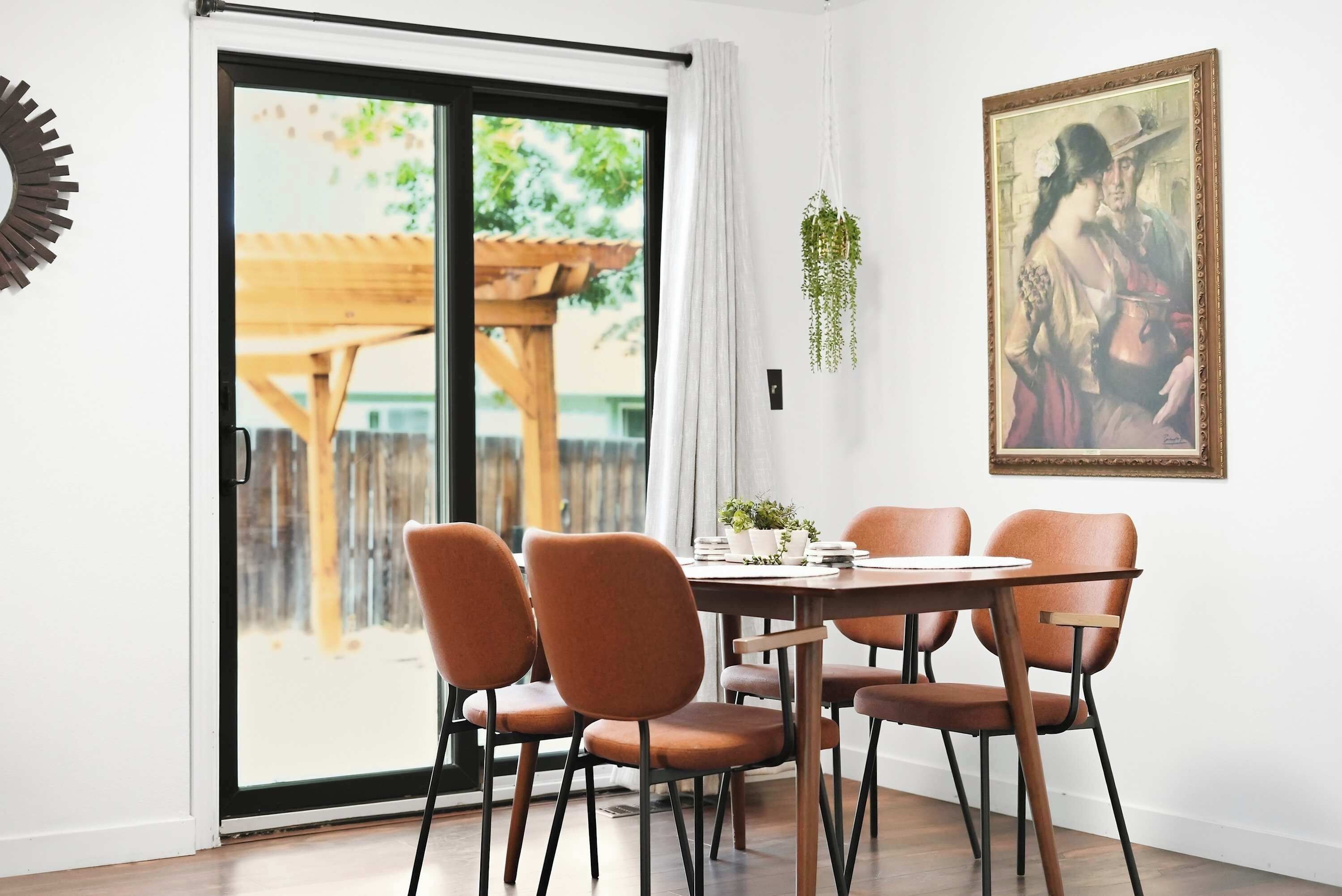 A dining area with a table and chairs, a sliding glass door leading to an outdoor space, and a framed painting on the wall.