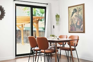Een eetgedeelte met een tafel en stoelen, een schuifdeur naar buiten en een ingelijst schilderij aan de muur.