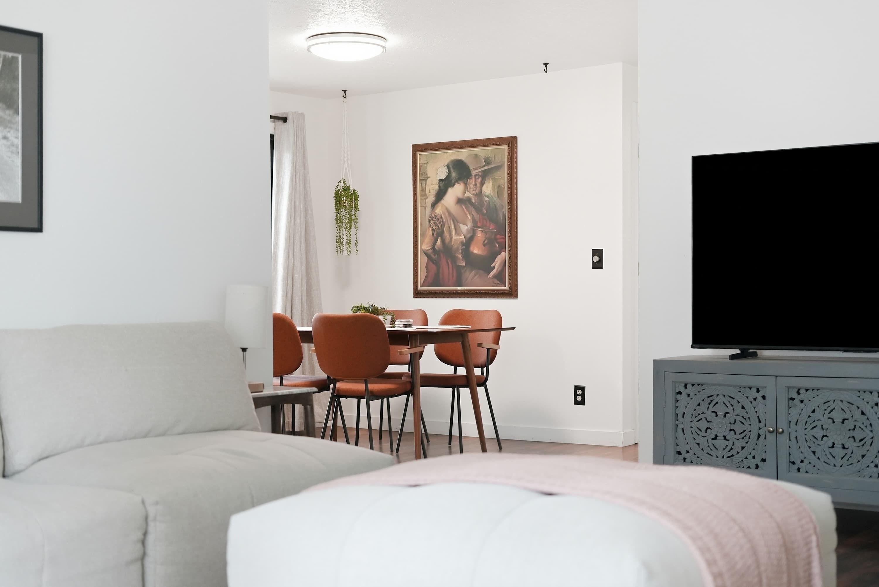 Een moderne woonkamer met een bank, een eettafel, stoelen, een televisie en een schilderij aan de muur.