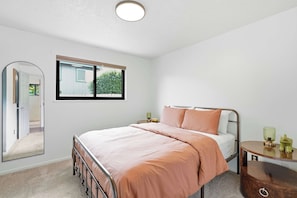 A bedroom with a bed, a bedside table, a mirror, and a window.