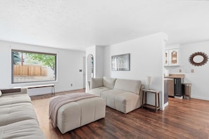 A modern living room with a large window, a sofa, a bench, and a small table.