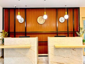 Un área de recepción con paneles de madera, tres relojes de pared y mostradores de recepción de mármol.