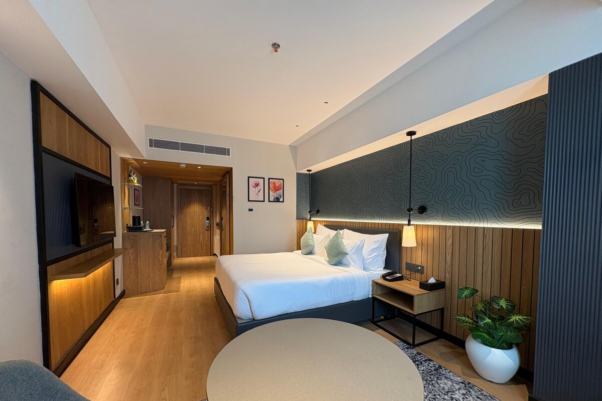 Una habitación de hotel moderna con cama, mesita de noche, televisor y una mesa redonda.