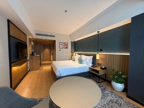 Una habitación de hotel moderna con cama, mesita de noche, televisor y una mesa redonda.
