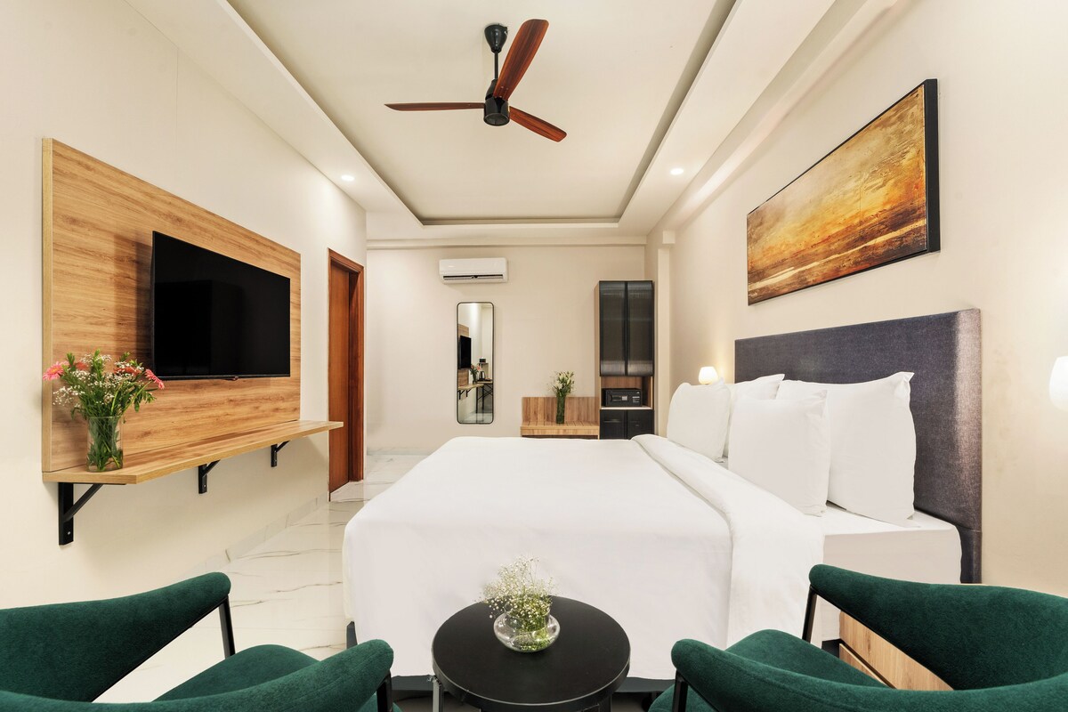 A modern hotel room with a large bed, a flat-screen TV, a ceiling fan, and a painting on the wall.