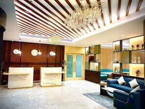 Un moderno vestíbulo con mostrador de recepción, zona de estar y elementos decorativos como un candelabro y relojes en la pared.