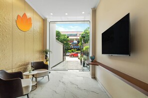 A hotel lobby with a TV, seating area, and a view of the street outside. - Country Inn Smart Stays Gurgaon (Gurugram)