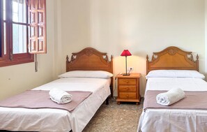 Ein Hotelzimmer mit zwei Einzelbetten, einem Nachttisch mit Lampe und einem Fenster mit Holzklappläden.