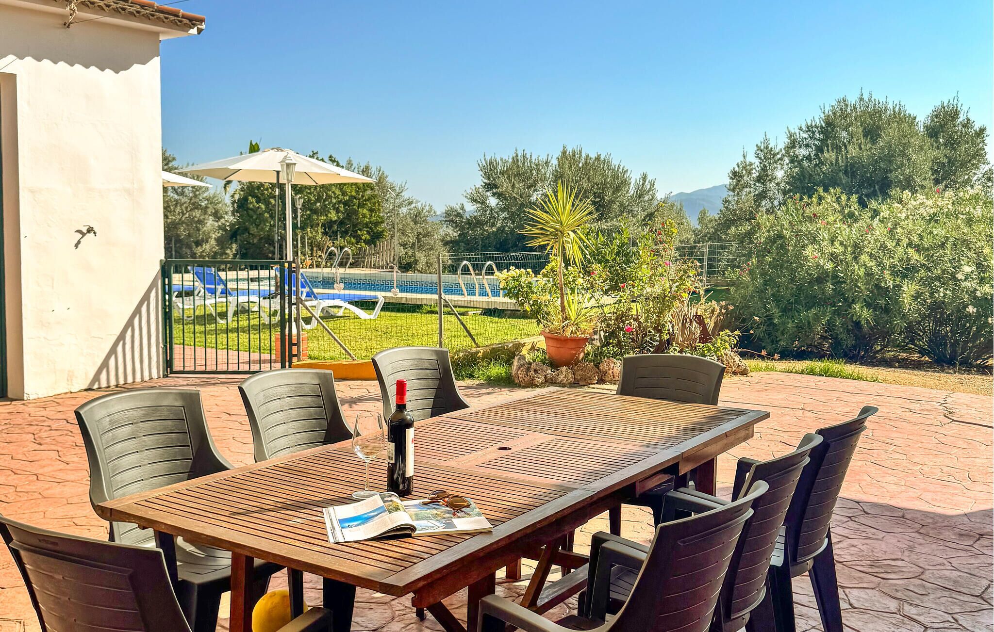 Eine Terrasse im Freien mit einem Holztisch und Stühlen, einer Weinflasche und einer Zeitschrift.