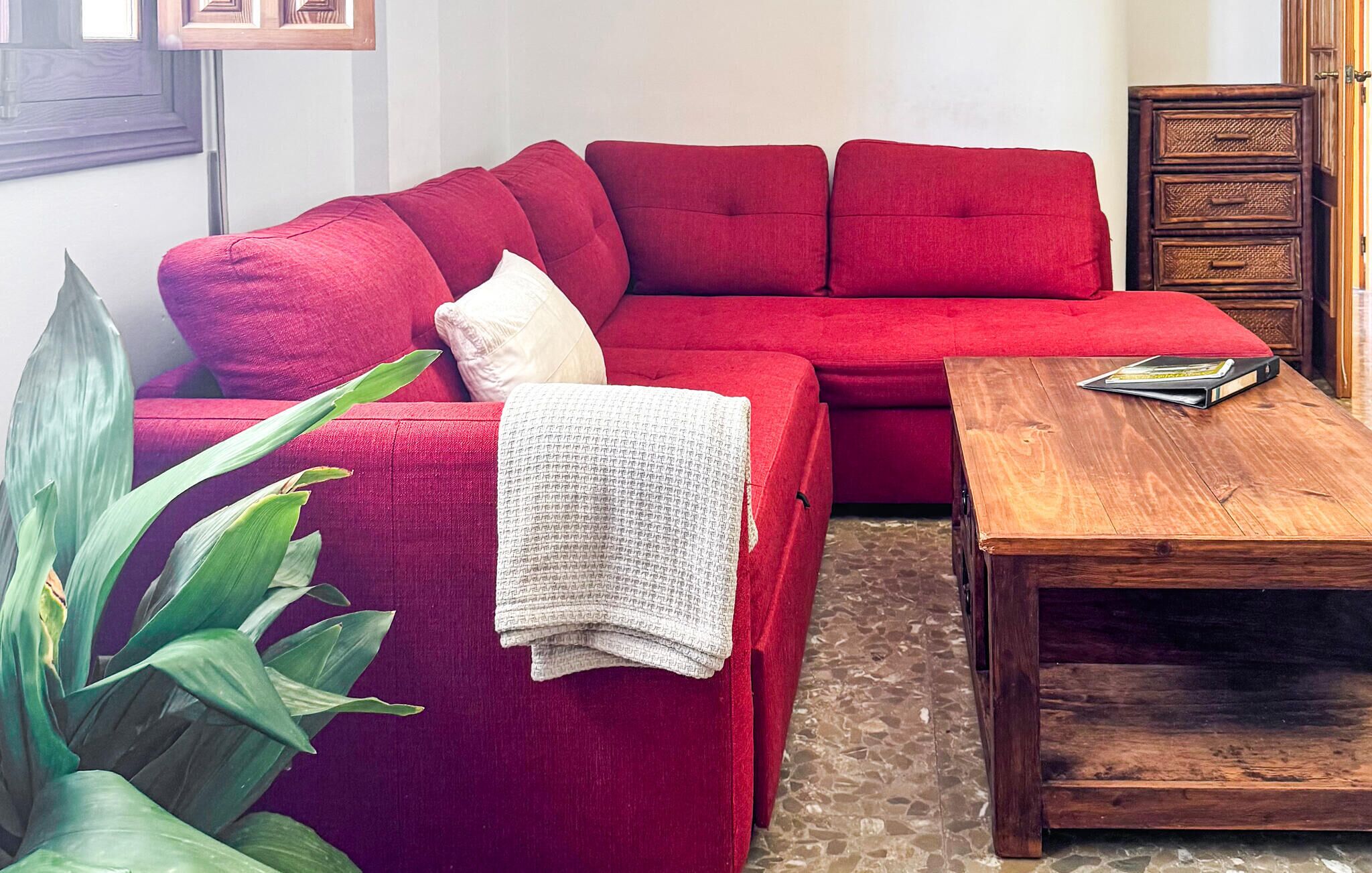 Ein rotes Sofa, ein Holztisch und eine Pflanze in einem Zimmer mit Fliesenboden.