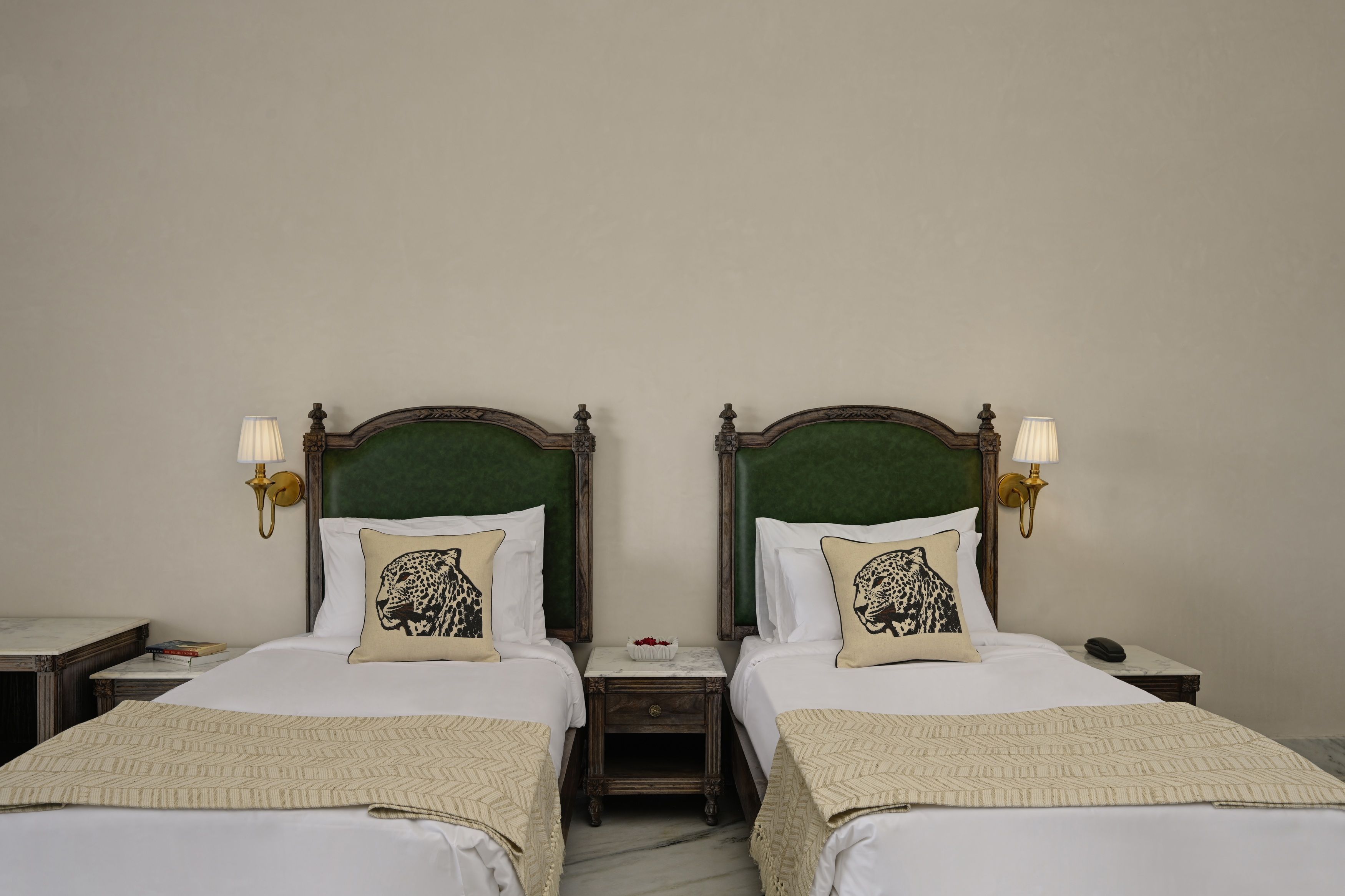 Dos camas individuales con cabeceros tapizados en verde, ropa de cama blanca y almohadones con estampado de leopardo.