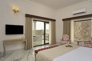 Een hotelkamer met een bed, een televisie, een bureau, een stoel, een klein tafeltje met een fruitschaal en een stenen muur.