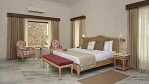 A hotel room with a large bed, two chairs, a small table, a stone wall, and a view of the outdoors. - Hari Bagh Jawai (Bali)