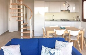 Un interior modern amb una escala espiraltraire, una zona de menjador amb taula i cadires, i una cuina amb armaris blancs i una estufa a gas.