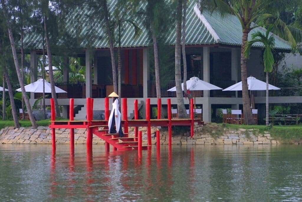 A waterfront property with a red dock, umbrellas, and a building with a green roof.