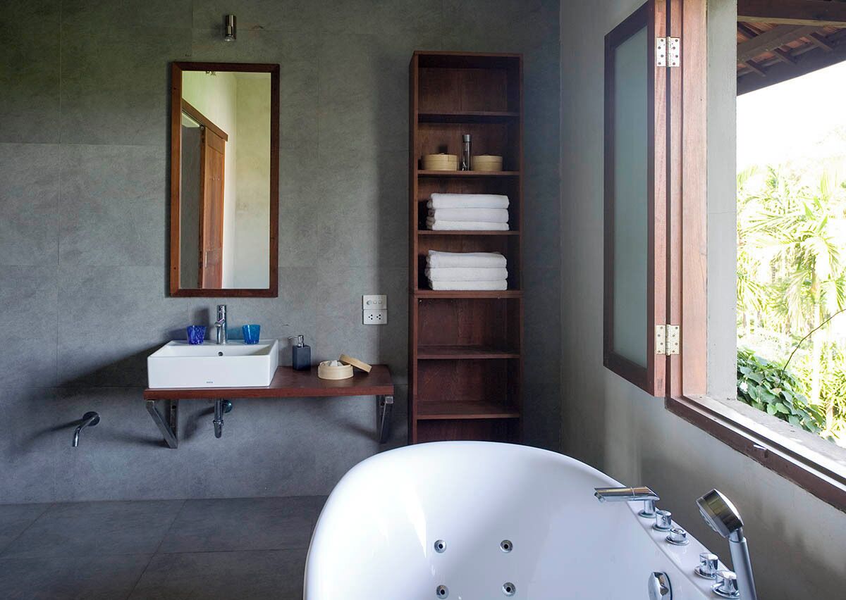 A modern bathroom with a freestanding bathtub, a wooden shelf with towels, a mirror, and a window with a view of greenery.