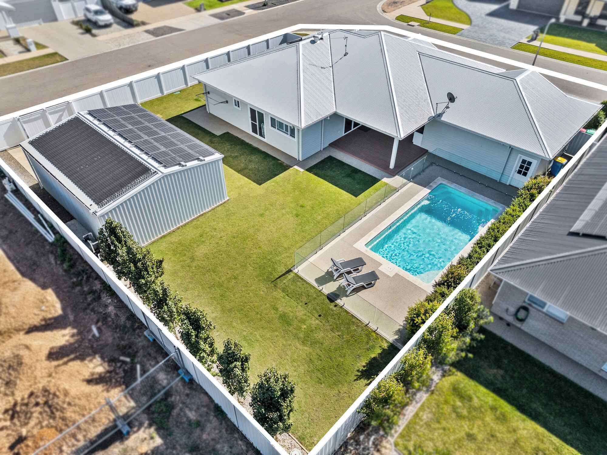 Ein Wohnhaus mit Swimmingpool, Solaranlage und umzäunter Garten.