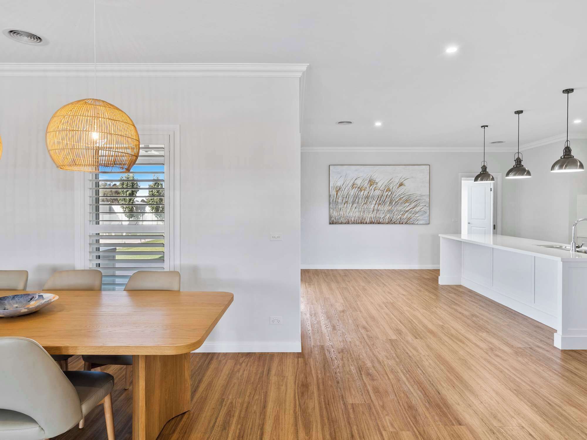 A modern kitchen with white cabinetry, a wooden dining table, and pendant lighting.