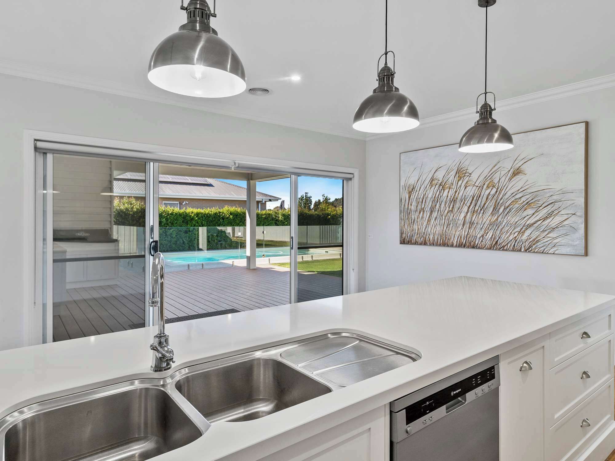 A modern kitchen with a large island, stainless steel sink, and overhead pendant lights.