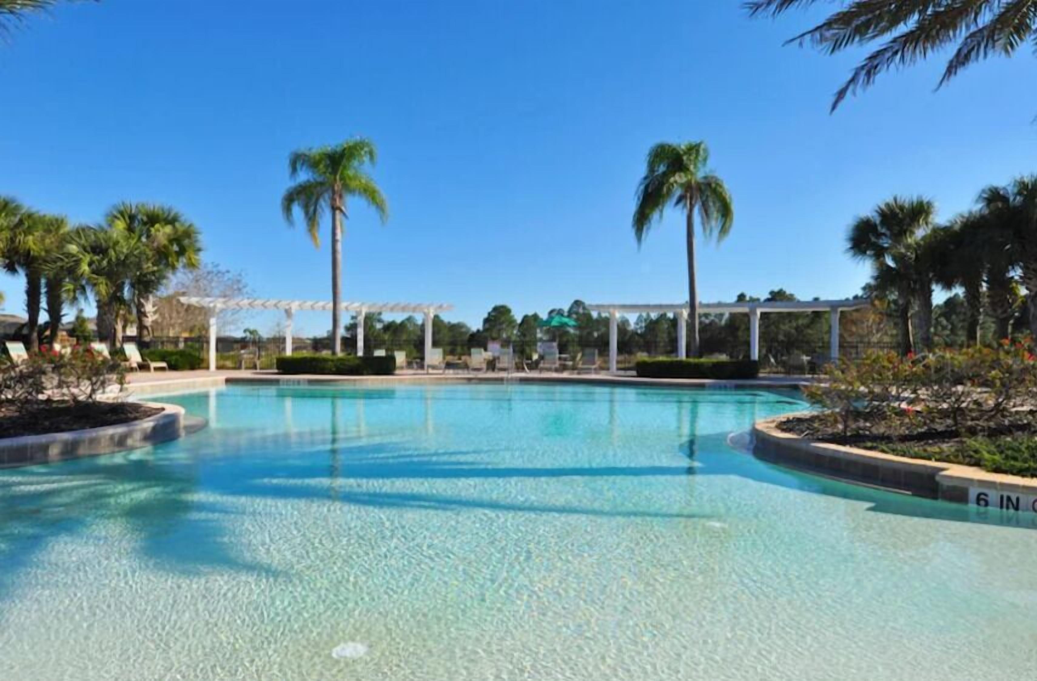 A clear blue pool with a pergola and palm trees in the background.