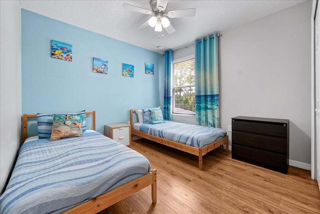 A bedroom with two beds, a ceiling fan, a window with curtains, and a dresser.