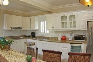 A kitchen with white cabinets, a granite countertop, a sink, a microwave, and a refrigerator. - 
4BR VIP Villa with Private Pool, Gold band, Chef & Golf Cart, Puerto Plata, DR (Puerto Plata)