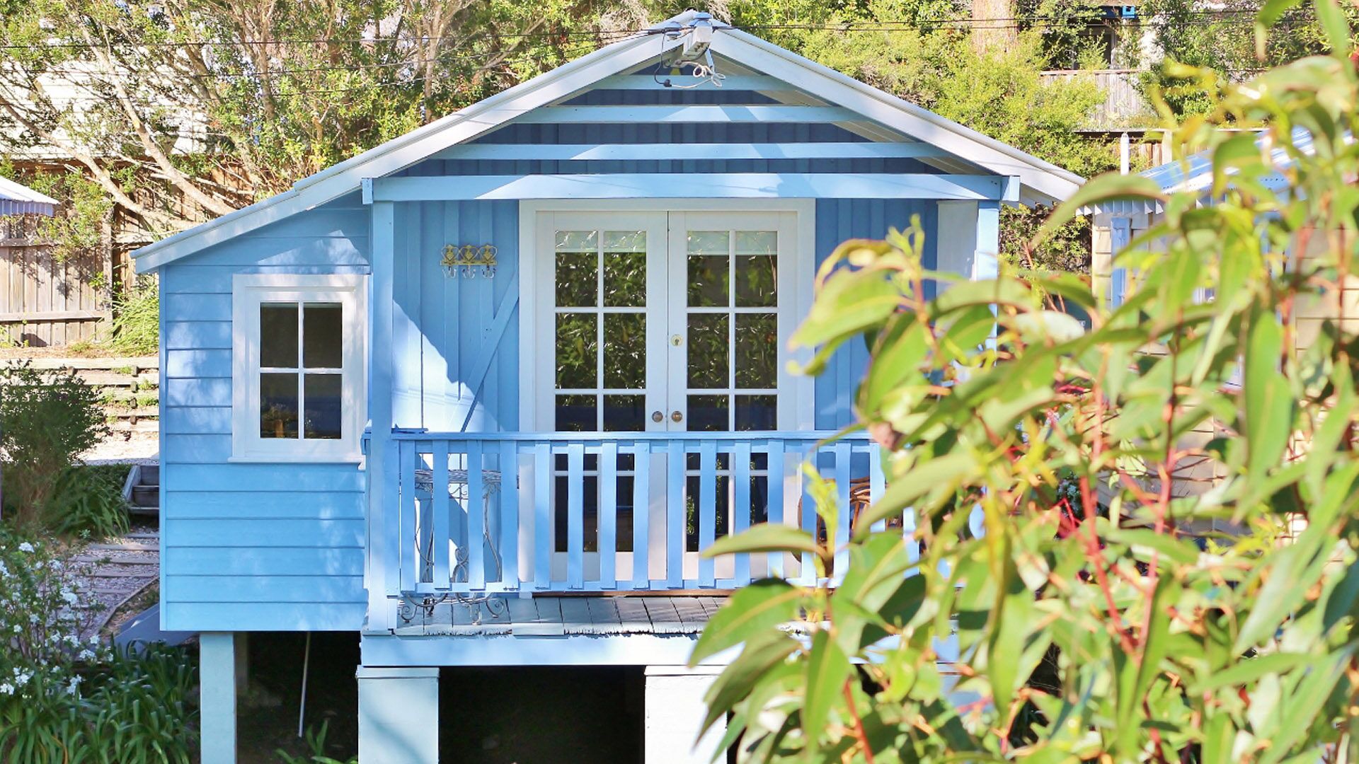 A small, single-story building with a blue exterior, a white door, and a small porch with a railing.