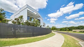 A modern two-story house with a curved roofline, a dark fence, and a well-maintained lawn. - Habitat - Lush Lennox Head Apartment (Lennox Head)