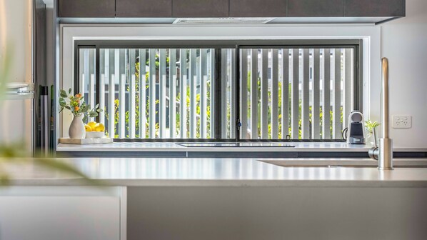 A kitchen with a large window, a vase with flowers, and a coffee machine.