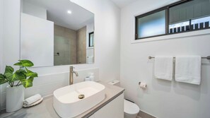 A modern bathroom with a freestanding bathtub, a large mirror, a toilet, and a window above the sink. - Habitat - Lush Lennox Head Apartment (Lennox Head)